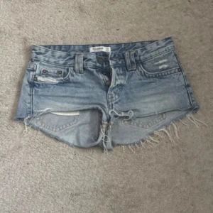 Blå jeansshorts från Pull&Bear - Snygga lågmidjade jeansshorts från Pull&Bear i storlek 34. De har låg midja, slitna detaljer och fransig kant nertill. Perfekta för sommardagar och festivaler. Oanvända då det tyvärr är för stora, annars hade jag behållt! 🩷