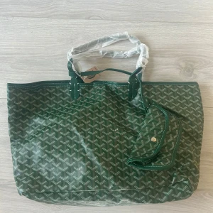 Grön handväska  - Säljer en grön handväska med ikoniskt grafiskt mönster och vita detaljer. Väskan har två handtag, matchande innerficka med knapp och kommer med original gul dustbag. Utsidan är i slitstark syntet och insidan är ljus och rymlig. Hör av er vid minsta lilla fundering!👍🏼🙏🏻