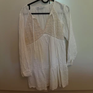 Vit kortklänning med spets från Zara - Supersöt vit kortklänning från Zara med långa ärmar och v-ringning. Köpt från förra sommarens kollektion. Använd endast fåtal gånger