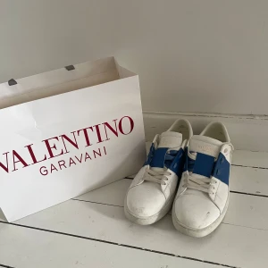 Valentino  Open  - Snygga Valentino Garavani Open sneakers i vitt skinn med bred blå läderdetalj. Perfekta för dig som gillar exklusiva och trendiga sneakers med unik design.Skorna är ej tvättade som ni ser så de mesta smuts bör försvinna efter en tvätt? Priset går självklart att diskuteras vid en snabb affär☺️