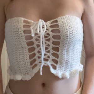 Handvirkad vit croppad tubtopp med snörning - Superfin handvirkad vit tubtopp med snörning framtill och i ryggen. Toppen är croppad och har volangkant nedtill. Mjuk och stretchig med snygga virkade detaljer. Priset är baserat på 50kr/h plus materialpris.