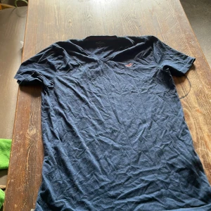 Mörkblå v-ringad t-shirt Hollister - Snygg mörkblå t-shirt från Hollister med v-ringning och liten broderad logga på bröstet. Klassisk passform och tillverkad i mjuk bomull, perfekt för en chill och stilren look.