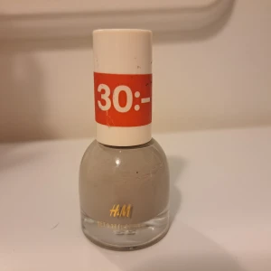 H&M nagellack Mushroom gråbeige - Nagellack från H&M i färgen Mushroom, en trendig gråbeige nyans. Kommer i en rund glasflaska med vit kork. Perfekt för dig som gillar neutrala och stilrena naglar.