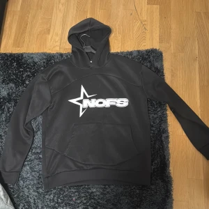 Svart NOFS hoodie med stjärntryck - Svart hoodie från NOFS i storlek M med stor vit stjärna och logga på bröstet. Klassisk känguruficka framtill och huva. Perfekt för dig som gillar streetwear och vill ha en enkel men snygg look.
