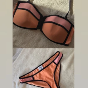 Färgstark bikini från Triangl - Säljer en snygg bikini från Frank dandy i orange och rosa med svarta kanter. Överdelen är bandeau-modell med  axelband och bygel, underdelen är klassisk trosa. Perfekt för stranden eller poolen!