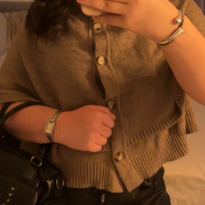 Beige kofta med knappar och ribbade kanter - Säljer en beige kofta med snygga knappar framtill och ribbade kanter. Koftan har en loose passform och är perfekt att slänga på sig över en t-shirt. Materialet känns mjukt och skönt, troligen ull eller en ullmix. Passar dig som gillar en chill och stilren look.