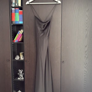 Svart långklänning med tunna axelband - Supersnygg svart långklänning med tunna axelband och draperad urringning. Klänningen har en slimmad passform och är tillverkad i ett glansigt, satinliknande material som ger en lyxig känsla. Perfekt för dig som vill sticka ut med en elegant och stilren look. Den är helt oanvänd!❣️