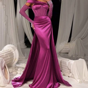 Lång lila satinklänning med pärldetaljer - Magisk långklänning i glansig lila satin med offshoulder och figurnära passform. Klänningen har en markerad midja, draperad kjol och matchande långa handskar med pärldetaljer. Perfekt för bal eller fest där du vill sticka ut.