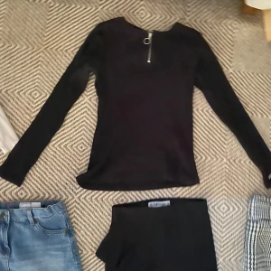 Svart långärmad tröja med dragkedja - Svart långärmad tröja med en snygg dragkedjedetalj vid halsen. Tröjan har en slim passform och är perfekt för lager-på-lager. Enkel och stilren design som funkar till många olika outfits.