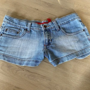 Ljusblå lågmidjade jeansshorts - (Pris går att diskutera❤️)Snygga ljusblå jeansshorts med klassisk femficksdesign och cool broderad bakficka i brunt och rött. Shortsen har låg midja, bälteshällor och slitna detaljer för en avslappnad vibe. Perfekta för varma dagar och enkel att matcha med allt.