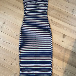 Randig ribbad klänning från Pieces NY  - Säljer en tight, ribbad klänning från Pieces i storlek M. Klänningen är lång, har horisontella ränder i blått, vitt, rött och ljusgult. Den är ärmlös och har en kroppsnära passform som framhäver siluetten. Perfekt för dig som gillar färg och mönster!