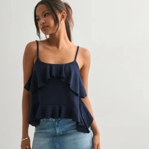 volang-linnetopp från Nelly  - En aldrig använd med prislappen kvar Supersöt mörkblå linne-topp med tunna axelband och dubbla volangdetaljer både fram och bak. Toppen är ärmlös och har en flowy, luftig passform som passar perfekt till jeans eller kjol. Materialet känns mjukt och lätt mot huden. Tidigare pris är 250 men jag säljer för 189