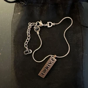 Dior J'adore halsband i silver - Snyggt halsband från Dior i silverfärgad metall med en rektangulär berlock där det står 'J'ADORE'. Kedjan har justerbar längd och detaljer med CD-logga. Perfekt statement-piece för dig som gillar lyxiga accessoarer. Nypris runt 3500 och jag köpte den på vestiere för 1100kr. Säljer  för ett jättebra pris på 700kr 💗💗💗