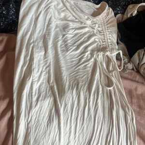 Vit tjol med slits och snörning - Supersnygg vit kortklänning med trendig snörningsdetalj på sidan som ger en cool rynkad effekt. Mjuk och lätt i materialet, perfekt för varma dagar. Enkel att styla med sneakers eller sandaler för en fräsch look.