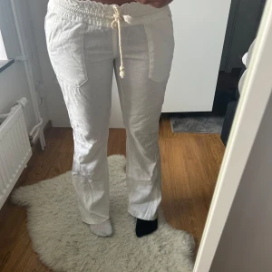 Vita linnebyxor från Roxy med snörning - Snygga vita linnebyxor från Roxy med avslappnad passform och breda ben. Byxorna har elastisk midja med grov snörning och stora fickor både fram och bak. Perfekta för chill dagar och sommarhäng.