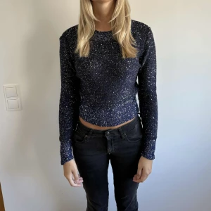 Mörkblå glittrig stickad tröja - Snygg mörkblå stickad tröja med glittriga inslag som ger en festlig känsla. Modellen är croppad och har lång ärm. Perfekt för dig som vill sticka ut lite extra med en glittrig touch. Tröjan är figurnära och har rund halsringning.