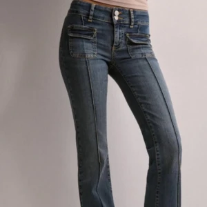Blå bootcut jeans med fickdetaljer - Blåa bootcut jeans med markerade sömmar längs benen. Mid waist med dubbla fickor fram. De är från Nelly och är köpta kring 1 år sedan. Säljer då de blivit för små och inte kommer till användning längre.