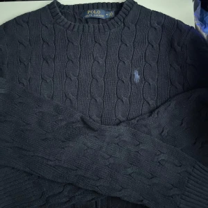 Mörkblå kabelstickad tröja Polo Ralph Lauren - Lite smutsigt har bara legat i garderoben i nån vecka,   Kabelstickad mörkblå tröja från Polo Ralph Lauren med klassisk rund hals och broderad logga på bröstet. Tröjan är långärmad och har en tidlös, stilren look som passar perfekt till jeans eller chinos. Skriv om du är intresserad eller vill ha mer bilder