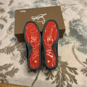 Christian Louboutin svarta mockasneakers - Snygga svarta sneakers från Christian Louboutin i mocka med ikonisk röd sula och diskret broderad logga på hälen. Skorna har snörning och en stilren, rund tå. Perfekta för dig som vill ha en lyxig och unik touch på din outfit.