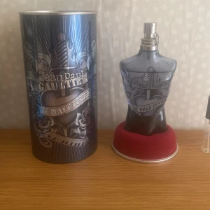 Jean Paul Gaultier Le Male Lover - Ungefär 110/125ml Cool parfym i form av en manlig torso från Jean Paul Gaultier, Le Male Lover edition. Flaskan är mörkgrå med tatueringsinspirerat mönster och levereras i en metallisk burk med matchande design. Perfekt för dig som gillar unika och snygga flaskor.