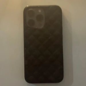 Svart quiltad mobilskal - Snygg svart mobilskal med quiltad yta och stilren design. Fodralet har rutmönster och är gjort i ett material som liknar mocka. Lite defekter med inget man riktigt tänker på fortfarande funktionell. Till iPhone 13 Pro