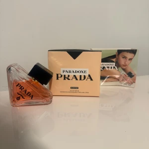 Prada Paradoxe Intense EdP 90ml - Prada Paradoxe Intense Eau de Parfum i en unik trekantig glasflaska med svart fyrkantigt lock. Doften kommer i en ljusbeige kartong med svart detalj och tydlig Prada-logga. Flaskan har en varm, bärnstensfärgad vätska och exklusiv design.