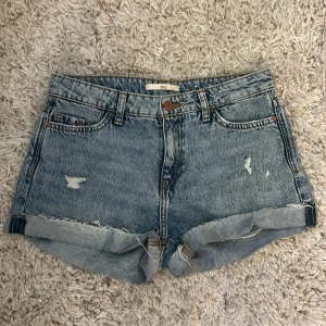EDC blå jeansshorts med slitningar - Snygga blå jeansshorts från EDC med rullade benslut och slitna detaljer framtill. Klassisk femficksmodell med knapp och dragkedja. Perfekta för sommaren och ger en avslappnad vibe. Passar dig som gillar en casual och trendig look.