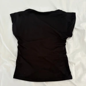 Svart backless top från Stradivarius XS - En svart, figurnära topp från Stradivarius i storlek XS. Toppen har korta ärmar och är tillverkad i ett stretchigt, stickat material som känns mjukt mot huden. Enkel och stilren design som är lätt att matcha med olika outfits.