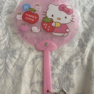 Hello Kitty rosa solfjäder - Söt rosa solfjäder med Hello Kitty-motiv. Fjädern har olika tryck med Hello Kitty, jordgubbar, rosetter och blommor. Handtaget är ljusrosa plast med liten kedja. Perfekt accessoar för att hålla sig sval och visa din kärlek till Hello Kitty. Ny 49kr/st 