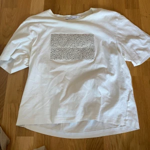 Vit t-shirt Calvin Klein Jeans - Vit t-shirt från Calvin Klein Jeans med svartprickigt mönster på bröstet och broderad logga. Klassisk passform, rund hals och korta ärmar. Tillverkad i mjuk bomull, perfekt för en clean och stilren look. Kan mötas upp i Trollhättan eller Alingsås. Kan skickas men då tillkommer en fraktkostnad.