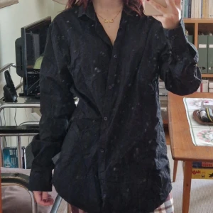 Svart skjorta i bomull, Premium Organic L - Klassisk svart skjorta i ekologisk bomull från Premium Organic. Skjortan har lång ärm, knappar framtill och en rak passform. Perfekt att styla oversized eller mer klassiskt. Enkel och stilren design som funkar till många olika looks.