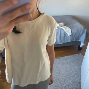 Vit topp med pärldetaljer på ärmar - Superfin vit topp i mjukt material med korta ärmar. Ärmsluten är dekorerade med glittrande pärlor och stenar som ger en lyxig känsla. Enkel rund halsringning och rak passform, perfekt för dig som gillar stilrena plagg med en twist.