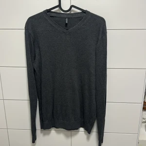 Mörkgrå stickad tröja Hampton Republic - Mörkgrå stickad tröja från Hampton Republic med v-ringad hals och lång ärm. Enkel och stilren modell som passar perfekt till jeans eller chinos. Mjuk och skön känsla, perfekt för kyligare dagar.