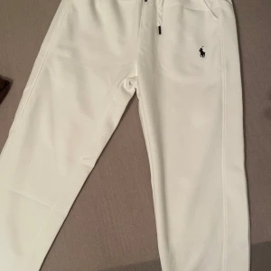 Vita mjukisbyxor från Polo Ralph Lauren - Snygga vita mjukisbyxor från Polo Ralph Lauren med klassisk broderad logga på höften. Byxorna har dragsko i midjan och är tillverkade i mjukt material för maximal komfort. Perfekta för en chill och stilren look.
