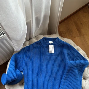 Blå ribbstickad tröja från H&M - En snygg blå ribbstickad tröja från H&M med högre rund halsringning. Tröjan har lång ärm och är gjord i ett mjukt, stickat material som känns både trendigt och bekvämt. Perfekt att styla med jeans eller kjol för en cool look.