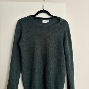 Mörkgrön stickad tröja från Vila - Mysig mörkgrön stickad tröja från Vila med rund halsringning och långa ärmar. Tröjan har en enkel och stilren design med ribbade muddar vid ärmslut och nederkant. Perfekt för lager-på-lager under kyliga dagar.
