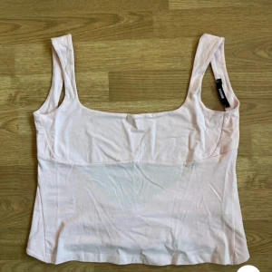 Ljusrosa omlottopp från BikBok - Supersöt ljusrosa omlottopp från BikBok med breda axelband och fyrkantig ringning. Toppen har knytband i ryggen för en snygg passform så den passar även xs. Perfekt att styla med jeans eller kjol för en trendig look.