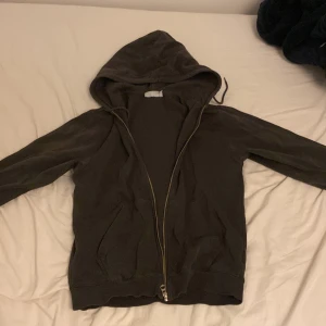 Svart hoodie med dragkedja från Weekday - En svart hoodie från Weekday i storlek XS. Tröjan har huva, dragkedja framtill och två fickor. Tillverkad i mjuk bomullsmix, perfekt för chill dagar eller när du vill ha en enkel och clean look. Långärmad och klassisk passform.