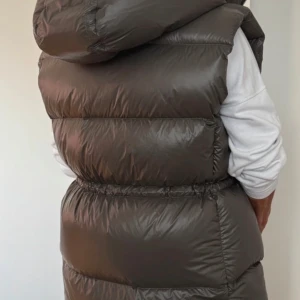  dunväst från H&M - Säljer en  dunväst från H&M med huva och dragsko i midjan. Västen är perfekt för kyligare dagar och har en stilren design. Den är tillverkad av 100% polyamid med fyllning av 80% dun och 20% fjädrar.