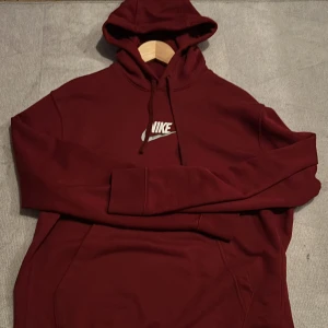 Vinröd hoodie från Nike - Säljer en snygg vinröd hoodie från Nike med klassisk logga på bröstet. Tröjan har en bekväm passform med långa ärmar och en praktisk magficka.