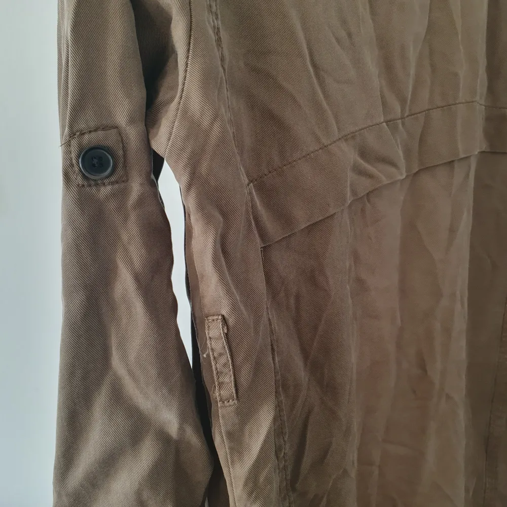 Säljer en snygg grön trenchcoat från Bershka i 100% lyocell. Jackan har långa ärmar och knappar på ärmsluten som kan vikas upp för en ny look. Mjukt tyg och trendig design. Bältet har fått fötter så det följer inte med. Litet slitage på flärpen på baksidan men det syns inte 💛 . Takit.