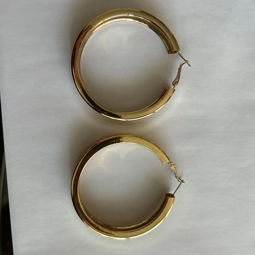 Snygga och stilrena guldiga örhängen i en klassisk rund design. Perfekta för att ge en elegant touch till vilken outfit som helst. Lätta att bära och matcha med andra smycken. 6cm i diameter . Asusteet.