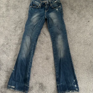 Bootcut jeans - Snygga blå jeans från Frankie Morello med slitna detaljer och broderad logga. De har en klassisk femficksdesign och en dragkedja med knappstängning. Perfekta för en avslappnad stil.