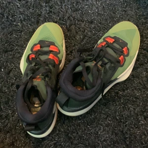 Gröna sneakers med röda detaljer - Snygga gröna sneakers med röda detaljer och svart snörning. Skorna har en vit sula med gummimönster undertill för bra grepp. Perfekta för en sportig look. Perfekta basket/ inomhus skor