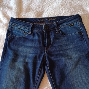 Blå bootcutjeans  - Snygga blå bootcut jeans med klassisk femficksdesign och knappgylf. Perfekta för en avslappnad stil med en touch av retro. De är bekväma och tyget är lite stretchigt. Midjemått 39-40 cm, innerbenslängd 76 cm. Superfint skick!!💓