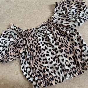 Offshoulder topp  - Snygg leopardmönstrad offshoulder topp från Gina Tricot. Toppen har korta puffärmar och elastiska kanter för en bekväm passform. Perfekt för att ge din outfit en vild touch! 🐆