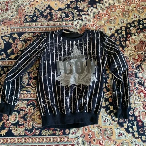 Svart och vit randig tröja från Dsquared2  - Säljer en cool svart och vit randig tröja från Dsquared2 med texten 'ICON' och ett stort lövtryck på framsidan. Tröjan är tillverkad i bomull och lycra för en bekväm passform. Perfekt för dig som vill sticka ut! Den passar även till storlek S