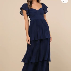 Marinblå långklänning med volanger - Helt ny, oanvänd med prislappar! Så fin plisserad balklänning från Lulus med volanger, knyts i ryggen med en söt rosett. Den är i stl L men passar mig som M perfekt💓 Nypris 1300kr