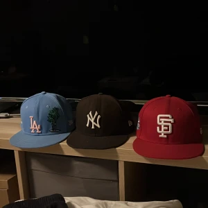 Tre kepsar från New Era - Säljer tre kepsar från New Era. En ljusblå med LA-logga och palm, en svart med NY-logga, och en röd med SF-logga.  150 kr styck eller 350 för alla 