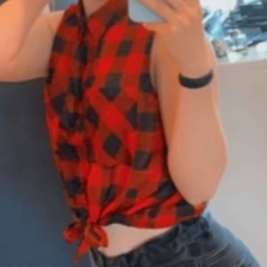 Rutig blus - Snygg röd och svart rutig blus med knyt framtill. Den är ärmlös och har en klassisk krage. Luftigt material! Perfekt för en avslappnad stil tillsammans med ett par svarta jeans! Använd enstaka gånger, kan fixa mer bilder vid önskemål!